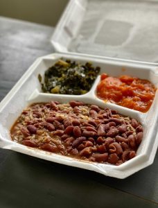 To-go container with greens, tomatoes, rice and beans